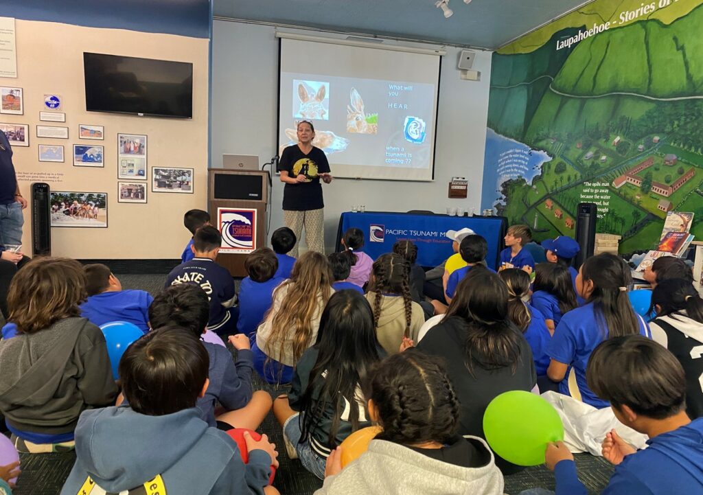 Pictured, a work learning about Earthquakes and Tsunamis with school students at the Pacific Tsunami Museum in Hilo, Hawaii.  With thanks to Dr Walter Dudley & Cindi Preller (featured)