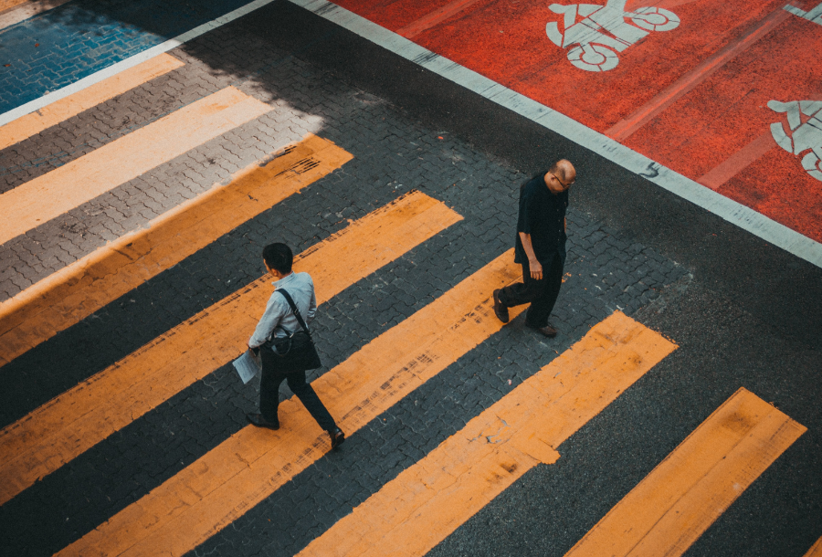 Picture of two men walking in opposite directions across an orange walk way crossing on the road