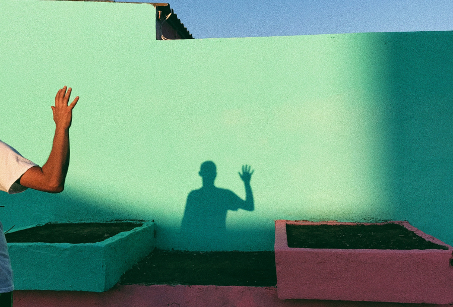 IMAGE DESCRIPTION: A beautiful muted green wall with a man standing on the far left hand side looking at this shadow on the wall from a distance