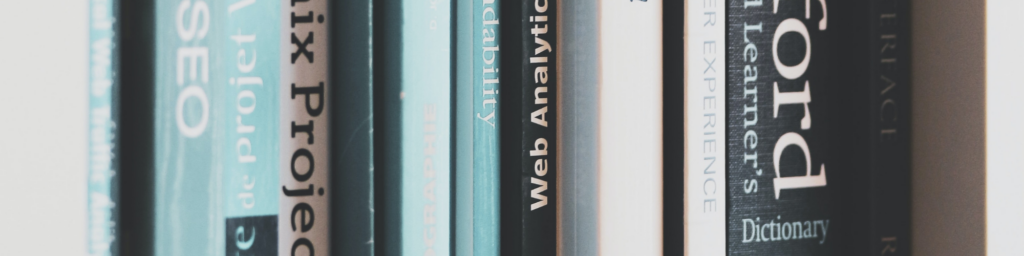 Pictured, multiple books in a white bookshelf with some highlighted being the Oxford Dictionary with a royal blue spine cover.