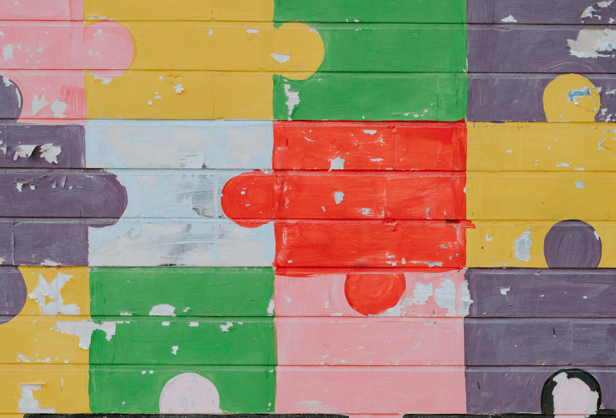 Pictured, a painted brick wall covered in bright coloured, bulky puzzle pieces in yellow, red, green and pink tones