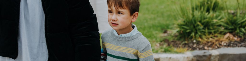 Picture of a small young boy wearing a grey striped jumper next to a woman wearing a big black jacket