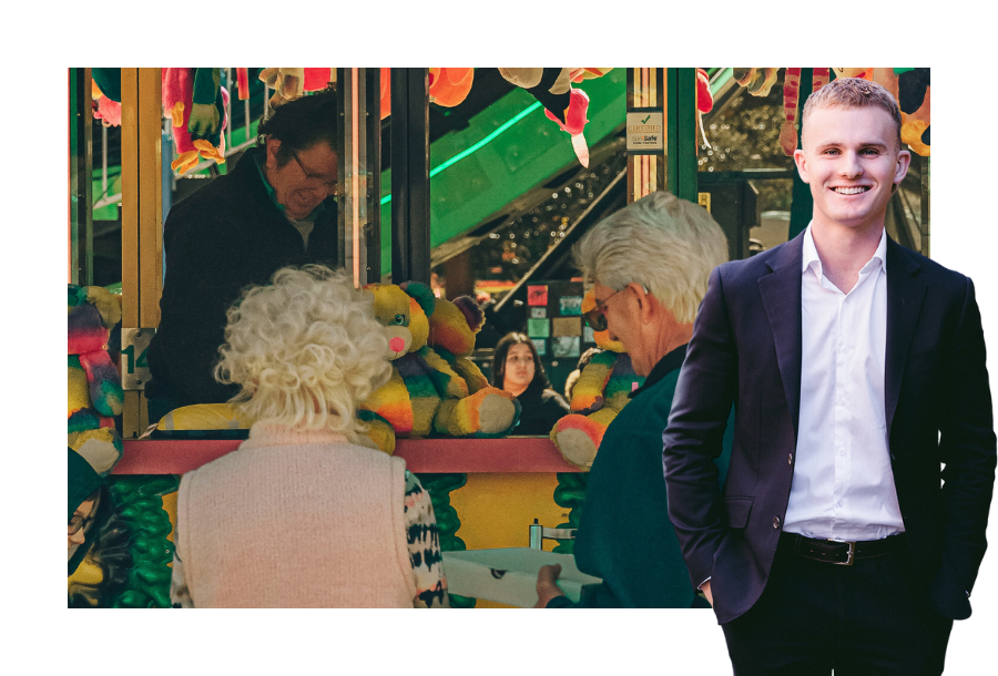 Jayden Scott wearing a black suit standing in front of a stock picture of an elderly couple looking to play a carnival game.