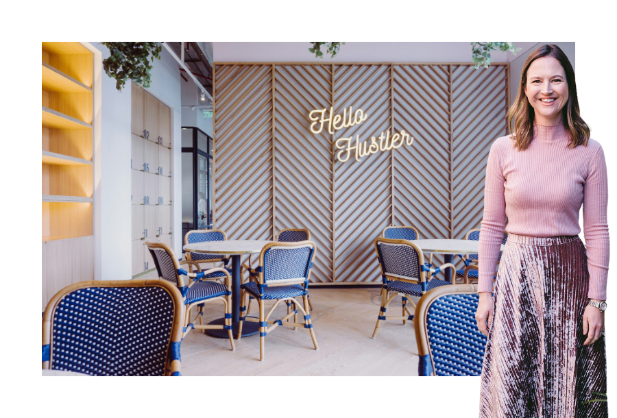 Pictured; Gabrielle Andersen standing smiling in a pink long sleeve shirt and long pink skirt. Behind her is an image of a small cafe style seating area with a neon sign that says "Hello Hustlers" on the back wall.