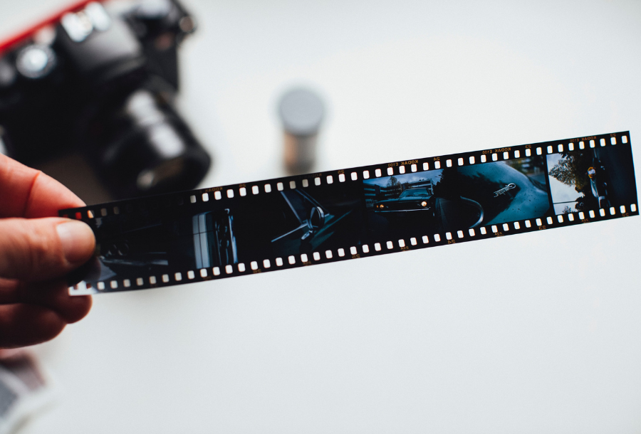 Pictured, a hand holding a photograph negative across the tile with a muted out SLR camera in the background