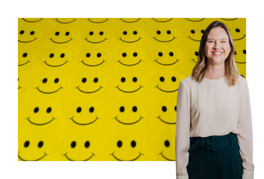 Pictured, Senior Solicitor Gabrielle Andersen standing in front of a stock picture of rows of joined bright yellow smiley faces