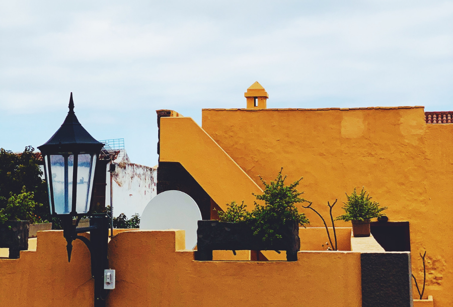 Yellow brick house in the background with a black style garden light at the forefront left hand side, rustic coloured yellow with some greenery on the different levels