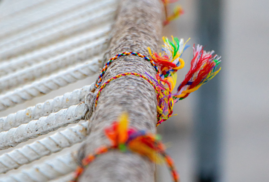 Bright coloured friendship bracelets tied to a metal fence with frayed edges at the tied ends - beautiful reds, purples, yellows and green colours shine through