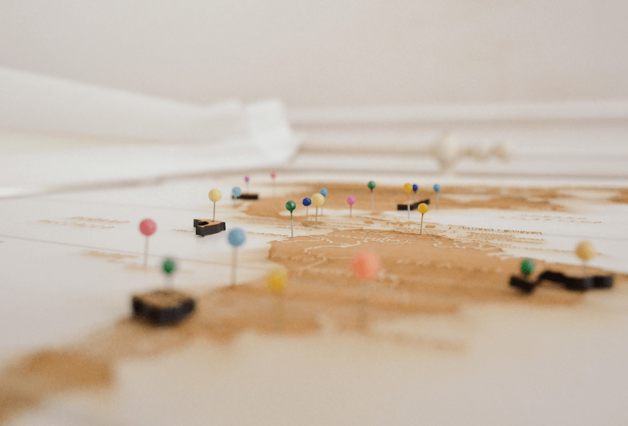 Flat lay of a world map outlined in muted dust colour, surrounded by different colours pins