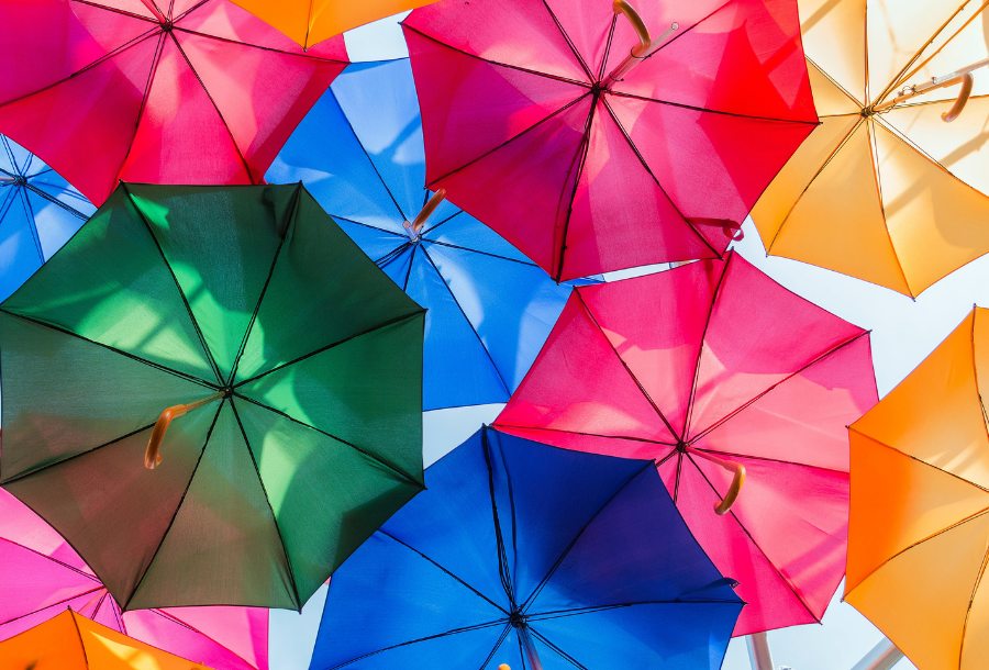 Looking up at a beautiful group of coloured umbrella's open against the bright blue sky with colours beaming from green, pink, yellow to blue