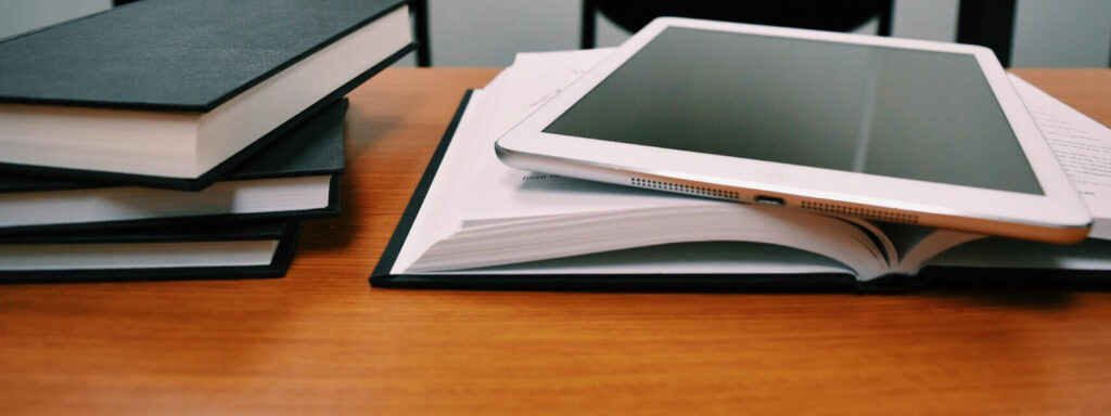 Books and an iPad on a desk to highlight studying. Graduates from teaching or nursing may be eligible to claim the HECS-HELP Benefit.